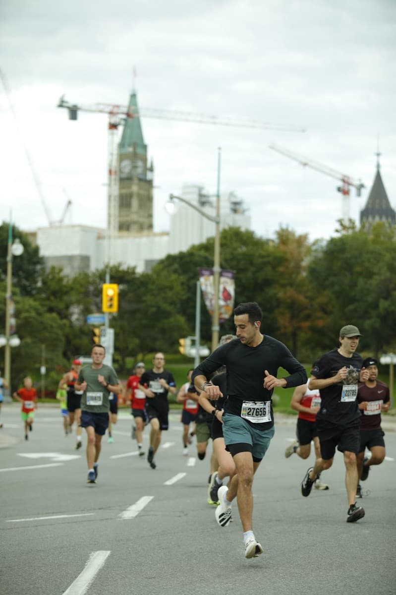 Running the Army Run 5K through downtown Ottawa in a black long-sleeve, Parliament Hill's Peace Tower and construction cranes rising behind the course